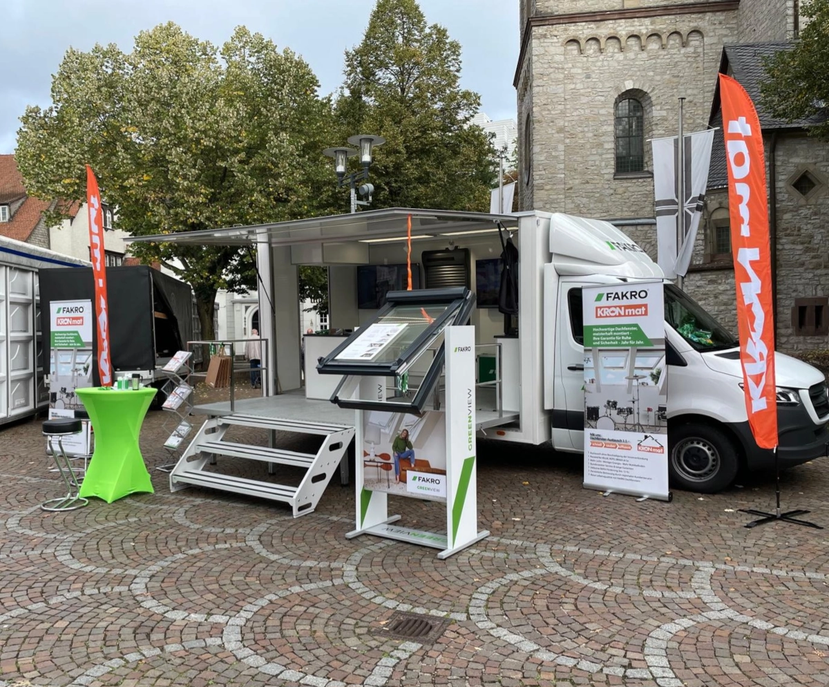 Mobiler Showroom von FAKRO und KRONmat auf einem Stadtplatz mit Bannern, Infoständern und ausgestellten Dachfenstern.